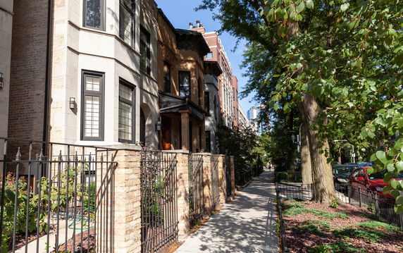 Front view of a multi-story brick townhouse with large windows and a wrought iron fence.
