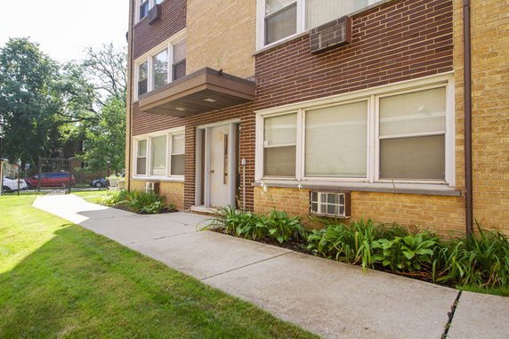 Front view of a brick apartment building with large windows and a small entrance canopy.