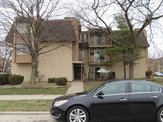 Front view of a multi-story residential building with a sloped roof and balconies.