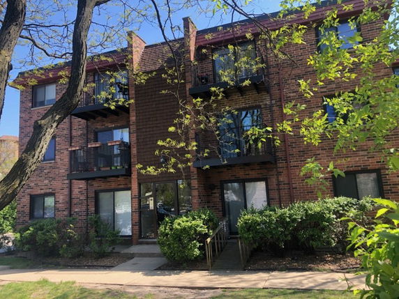 Front view of a three-story brick apartment building with balconies.