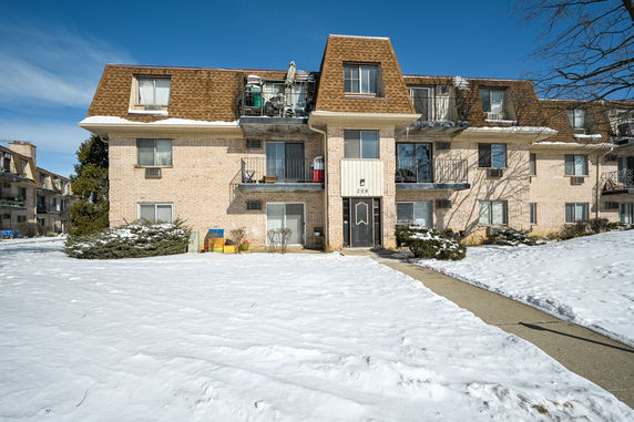 Front view of a three-story apartment building with balconies and a snow-covered yard.
