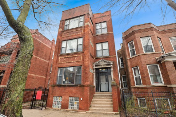 Front view of a three-story brick building with a central entrance and steps leading up to it.