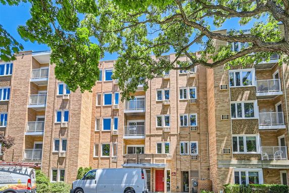 Front view of a multi-story brick apartment building with balconies and a red entrance door.