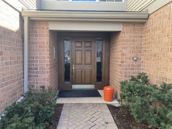 Front view of a house entrance with a wooden door and brick walls.