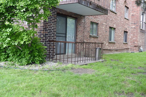 Side view of a brick apartment building with a small fenced patio area.