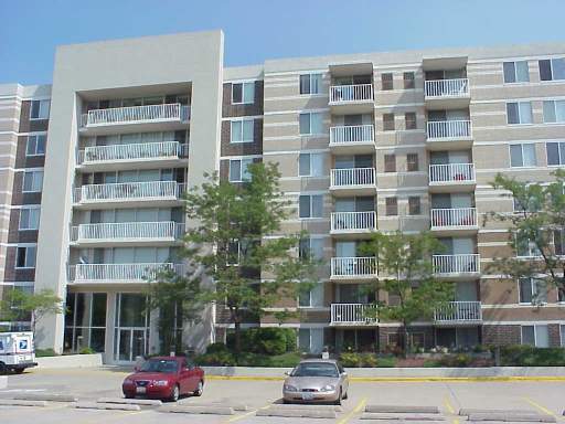 Front view of a multi-story apartment building with balconies and parked cars in front.