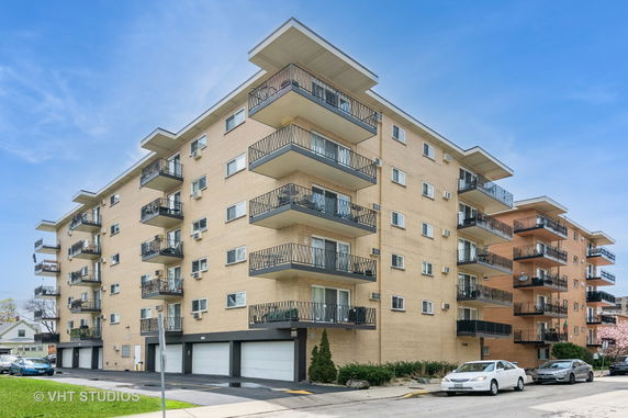 Front view of a multi-story apartment building with beige brick exterior and balconies.
