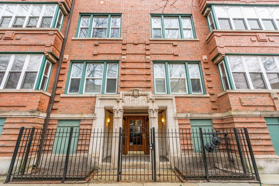 Front view of a brick apartment building with green-framed windows and a gated entrance.