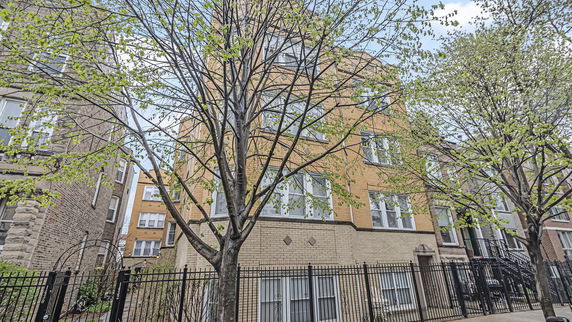Front view of a multi-story brick building with several windows and a fenced yard.
