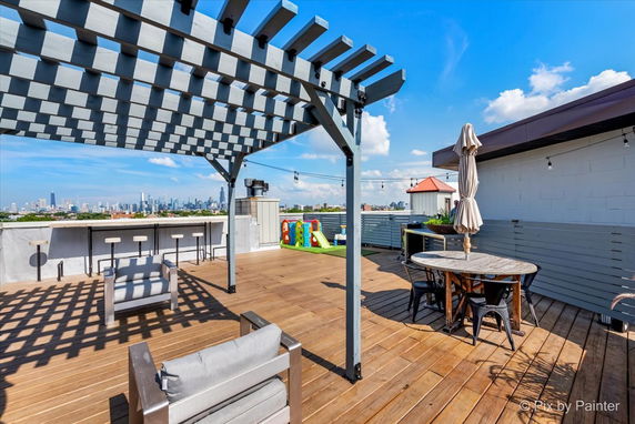 Rooftop area with seating, play structure, and pergola overlooking a city skyline.