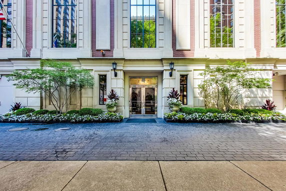 Front view of a building entrance with decorative plants and large windows.