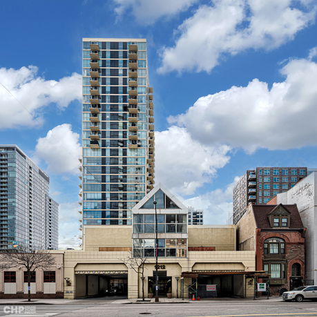 Front view of a high-rise building with multiple balconies and a glass entrance section.