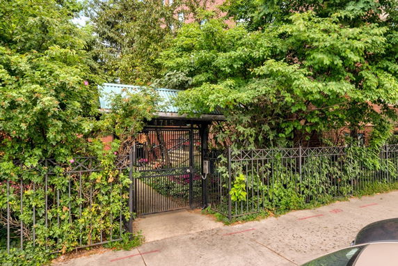 Front view of a gated entrance with greenery and brick building partially visible.
