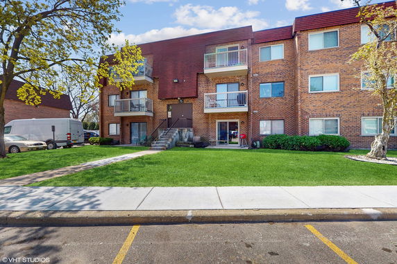 Front view of a three-story brick apartment building with balconies.