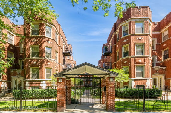 Front view of a multi-story brick apartment building with balconies and entrance gate.