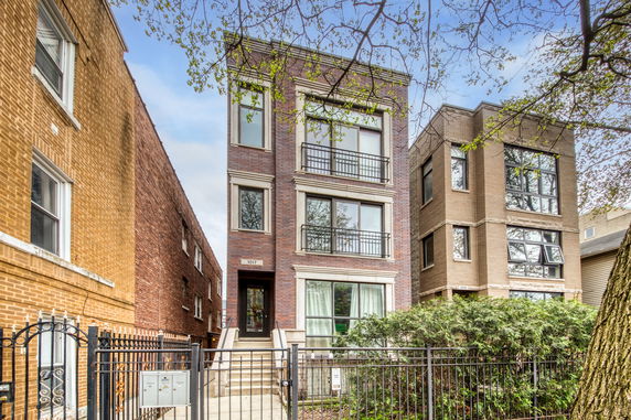 Front view of a three-story brick residential building with multiple windows and a gated entrance.