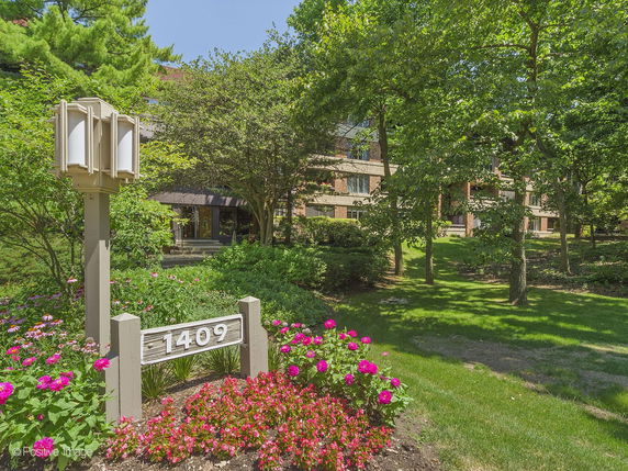 Front view of a building with multiple entrances, surrounded by trees and flowers.