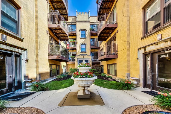 Front view of a multi-story building with balconies and a central fountain in the courtyard.
