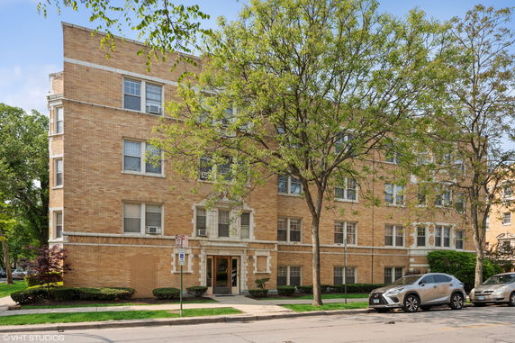 Front view of a multi-story brick apartment building with multiple windows and an entryway.