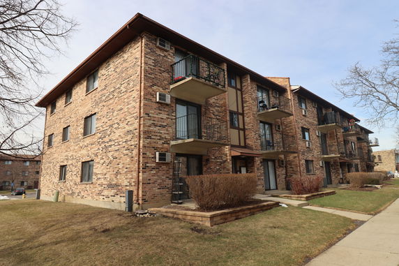 Front view of a multi-story brick apartment building with balconies.