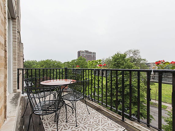 Balcony view with outdoor furniture overlooking green trees and a distant building.