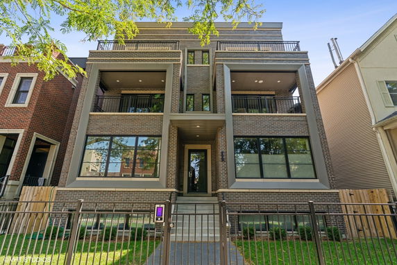Front view of a multi-story brick building with balconies and a central entrance.