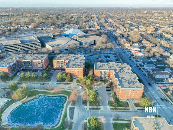 Panoramic view of a neighborhood with several apartment buildings, streets, and a small pond.