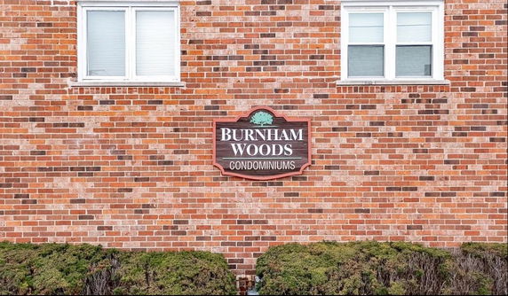 Brick exterior wall of a condominium building with two windows and a sign reading 'Burnham Woods Condominiums'.