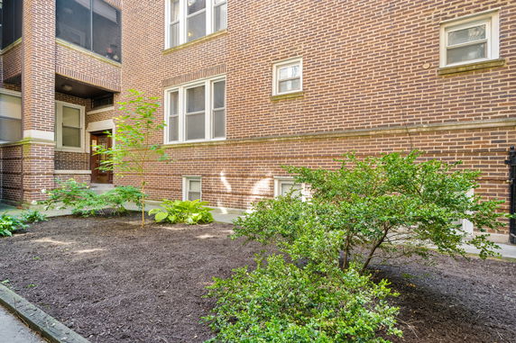 Exterior view of a brick apartment building with windows and a garden area.