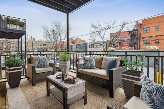 Outdoor seating area on a balcony with views of surrounding buildings and trees.