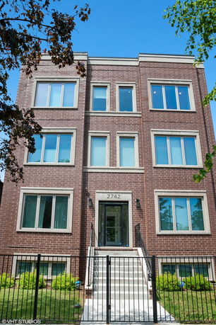 Front view of a multi-story brick building with large windows and a gated entrance.