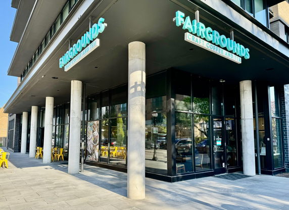 Street view of a modern building with large glass windows and a cafe on the ground floor.