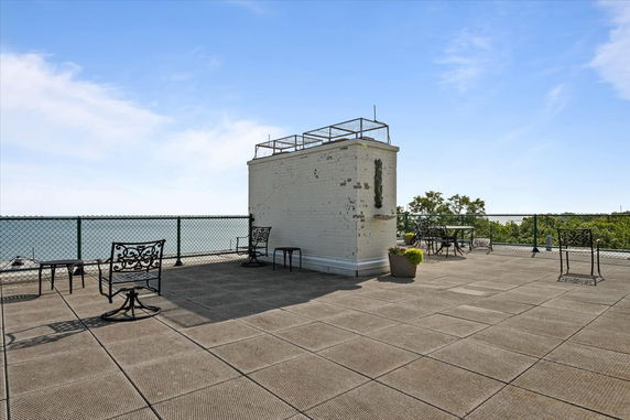 A spacious rooftop with metal chairs, tables, and potted plants.