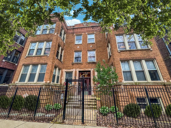 Front view of a brick multi-story residential building with large windows and a gated entrance.