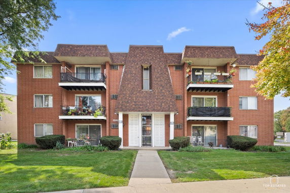 Front view of a three-story brick apartment building with balconies.