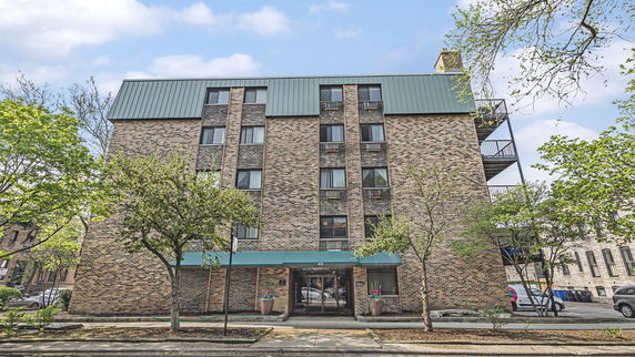 Front view of a multi-story brick apartment building with a green roof and an entrance canopy.