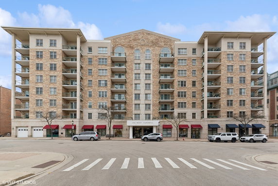 Front view of a multi-story apartment building with balconies and commercial storefronts on the ground level.