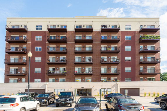 Front view of a multi-story apartment building with balconies and parking area.