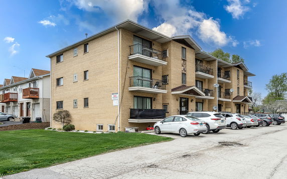Front view of a multi-story apartment building with balconies and parking area.