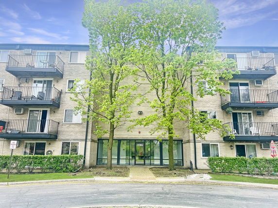 Front view of a multi-story apartment building with balconies and a central entrance.