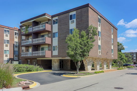 Front view of a four-story apartment building with balconies and a stone-covered ground floor.