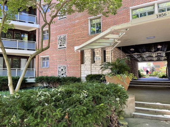 Front view of a multi-story apartment building with a brick facade and balcony railings.