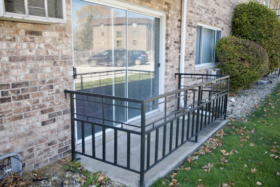 Front view of an apartment building with a sliding glass door and a metal railing.