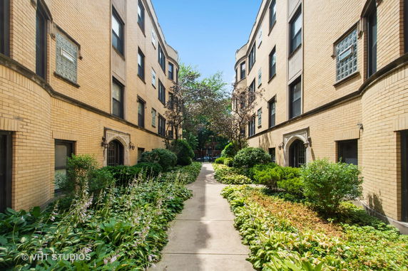 View of a walkway between two three-story residential buildings with a garden area.