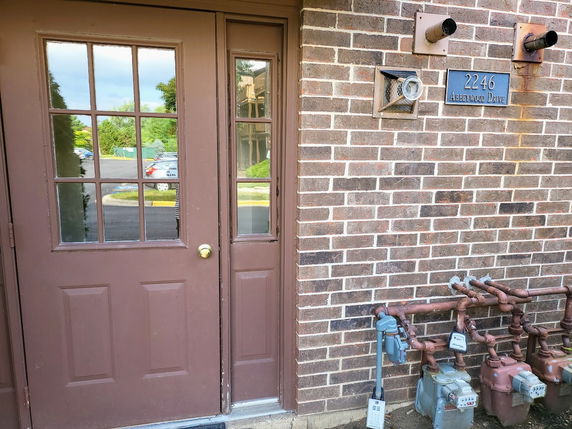 Front view of a building entrance with brown double doors and a brick wall.