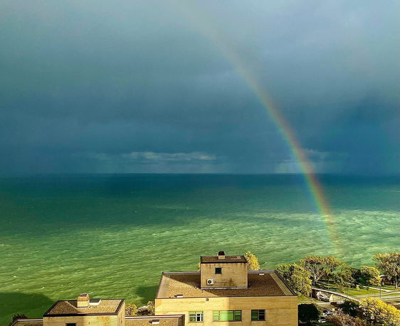Panoramic view of the ocean with a rainbow in the sky, rooftops of buildings in the foreground.