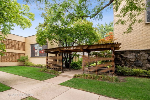 Front view of a building entrance with wooden pergola and brick facade.