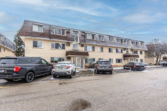 Front view of a three-story apartment building with a sloped roof and multiple parking spaces.