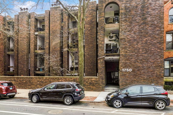 Front view of a brick apartment building with balconies and a street entrance.