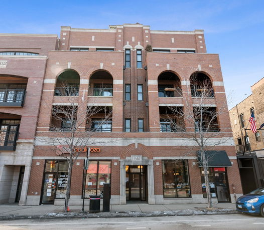 Front view of a multi-story brick building with arched balconies and commercial spaces on the ground floor.